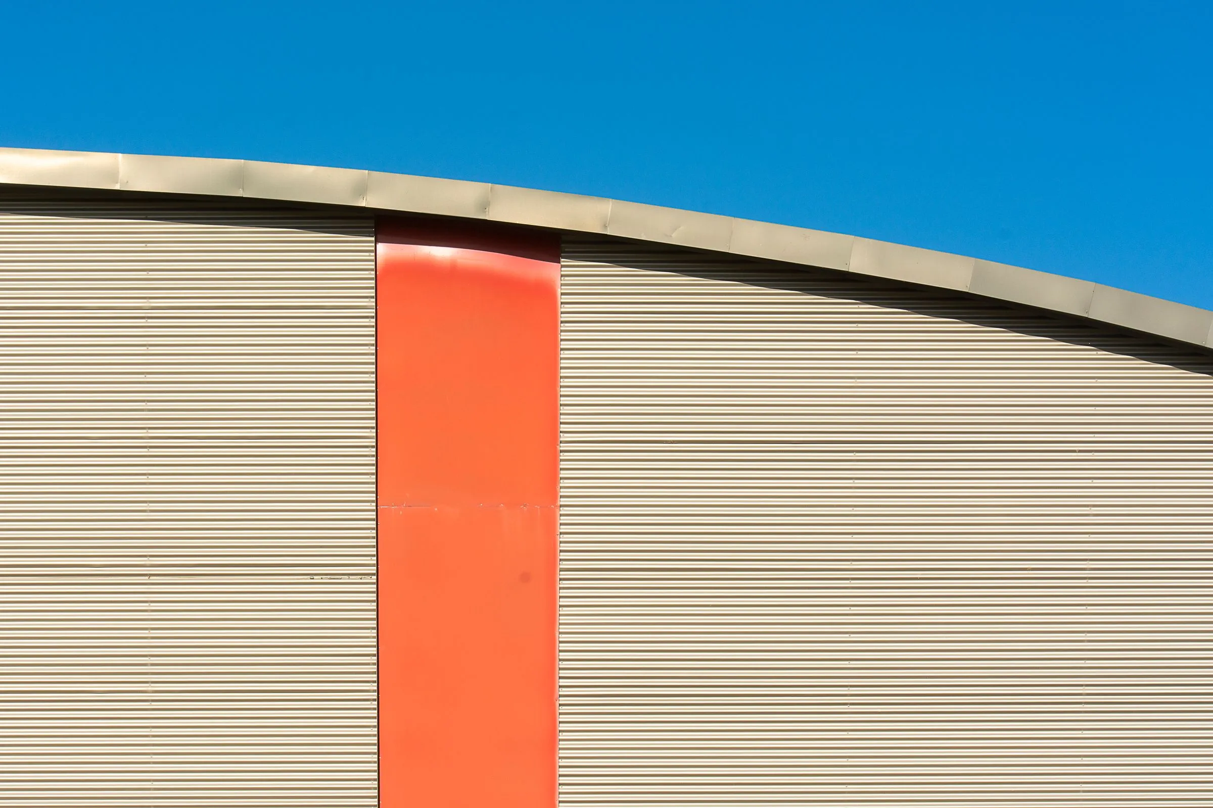Profiled panel wall with an orange stripe under a curved roof and blue sky